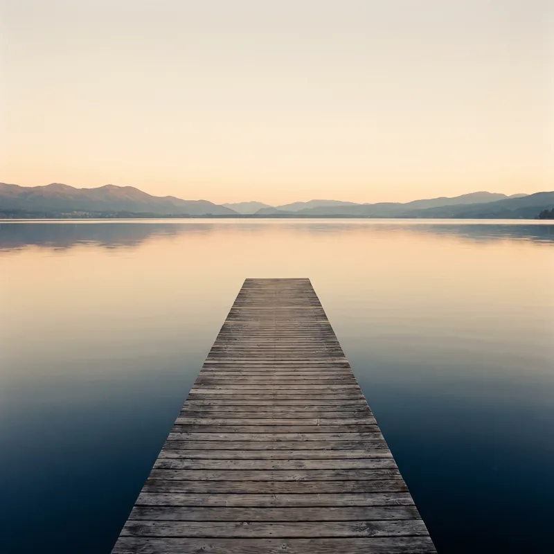 Un ponton de bois s’avance dans l’eau calme du lac, au lever du jour.